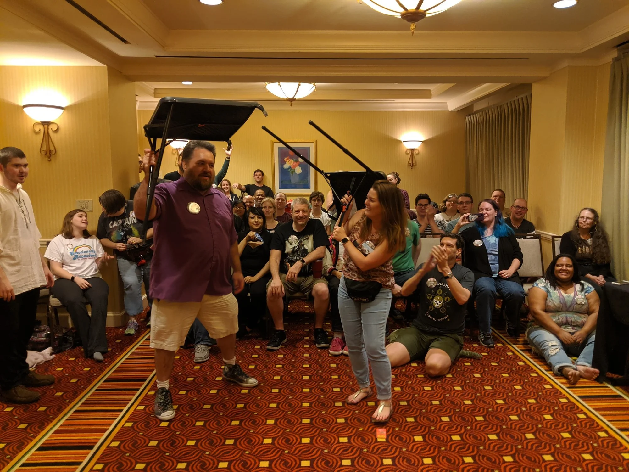 Table Flipping Championship at Board Game Bash - two competitors holding tables overhead with crowd watching and laughing